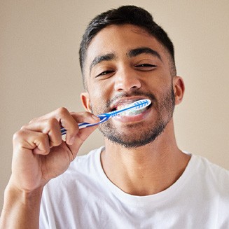 Man smiling while brushing his teeth