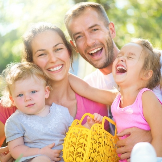 Family of four laughing outdoors on sunny day