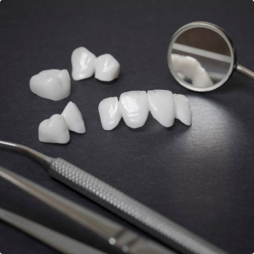 Several white dental crowns and veneers on table next to dental mirrors