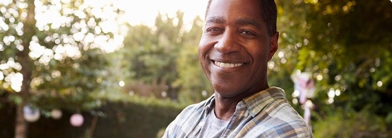 Man in plaid shirt smiling with trees in background