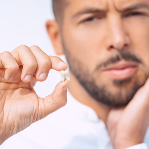 Man holding extracted tooth in one hand and touching his jaw with the other