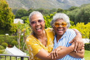 Two mature women smiling and embracing with a scenic hillside behind them