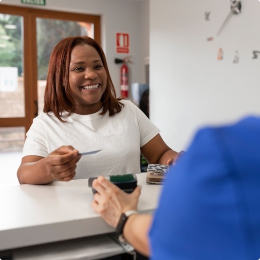 Woman handing payment card to dental team member at front desk